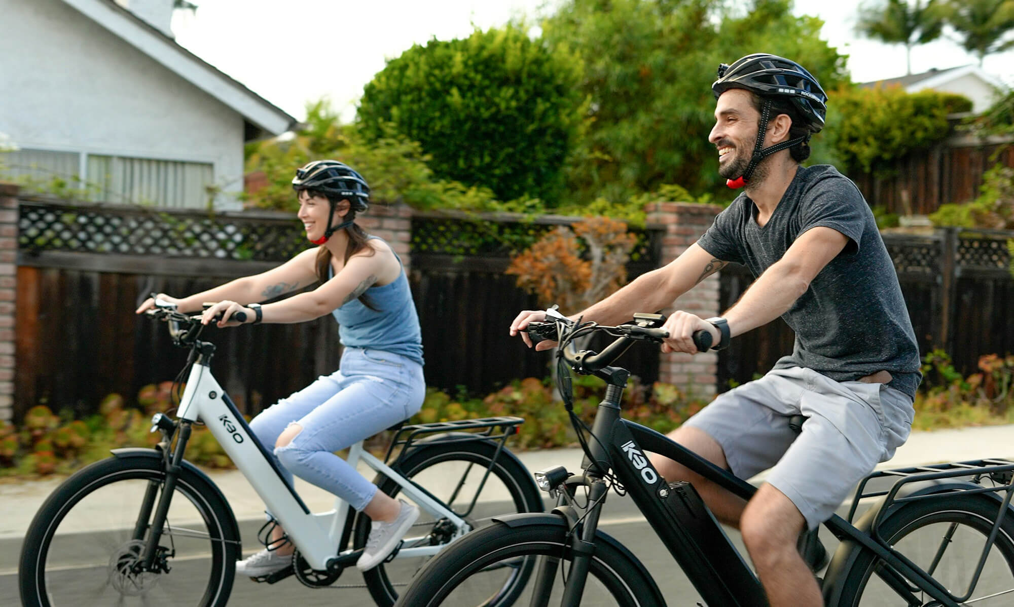 Två personer på elcyklar cyklar genom ett bostadsområde
