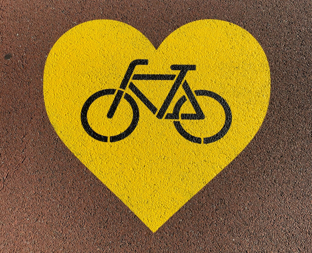 Ett gult hjärta ritat i asfalten med en svart cykel i