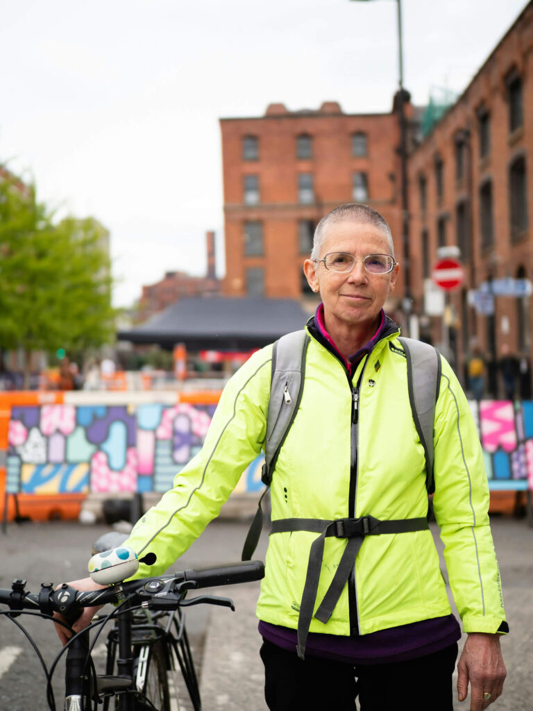 Ett porträtt på en person med funktionskläder och ryggsäck som håller i sin cykel i en stad